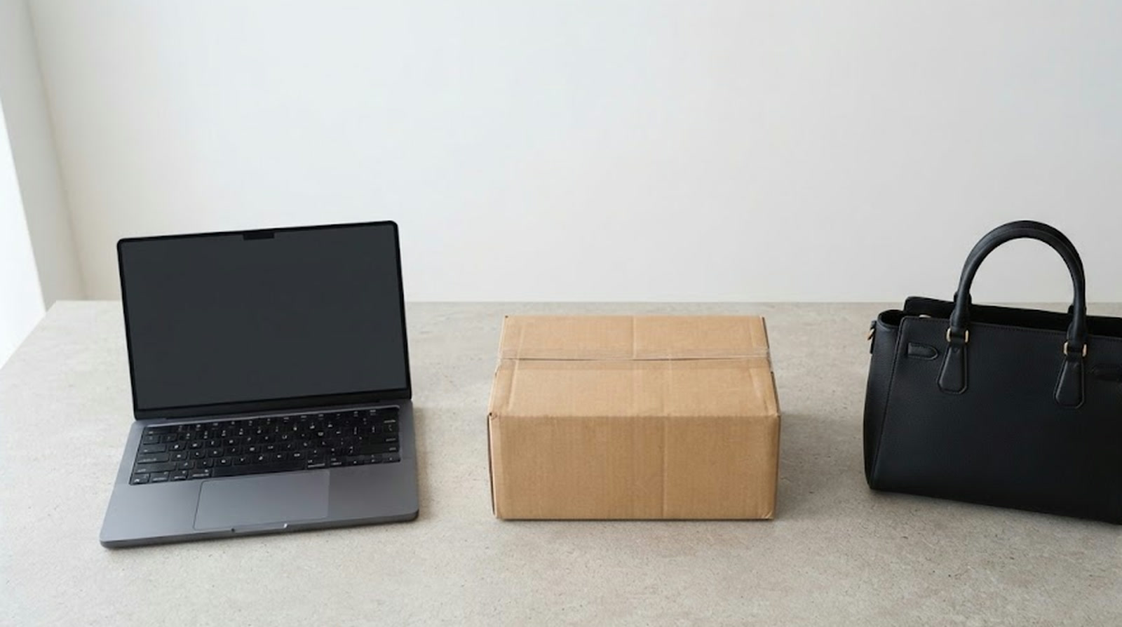 A laptop with a dark screen, one sealed shipping box and a black leather handbag on an otherwise empty tabletop, with no stock shelves behind them